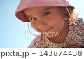 Young girl in pink hat smiles while holding tiny flower. Soft sunlight highlights her joyful expression. Focus on her hands delicately handling the bloom. Ideal for nature, childhood 143874438