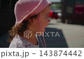 Young girl in pink hat holds toy hose near colorful fire truck. She looks focused, curious, and playful. Scene captures childhood innocence during outdoor playtime 143874442