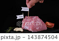 A male hand adds protein, iron, vitamin B12 and zinc labels to fresh raw pork surrounded by rosemary, garlic and pepper on black slate. Nutritional awareness concept 143874504