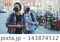 Young adults wearing protective masks using smartphone in urban square 143874512