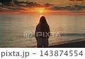 Woman standing and raising arms at ocean beach during sunrise 143874554