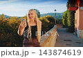 Blonde woman taking selfie on smartphone by stone wall with forest view 143874619