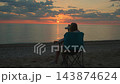 Woman sitting on camping chair drinking coffee at coastal beach sunrise 143874624