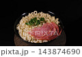 Instant noodles with sausage and parsley sit on a plate while a wooden stand rotates smoothly against a black background. Quick meal concept 143874690