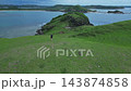 Woman Resting On Summit Watching Gentle Bay Beneath Lush Grassy Landscape 143874858