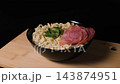 A plate of instant noodles with sausage and parsley turns on a wooden cutting board against black background. Prepared convenience food concept 143874951