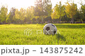 Soccer ball rests on sunlit grass in park at sunset. Warm sunlight creates peaceful outdoor sports mood. Closeup supports football, recreation, fitness, and healthy lifestyle content for campaigns. 143875242