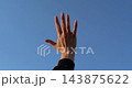 Raised hand waves against clear blue sky. Person reaches upward in bright daylight. Gesture suggests greeting, freedom, hope, or asking for help. Minimal outdoor footage offers useful copy space. 143875622