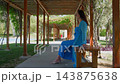 Woman in blue dress sitting on bench under wooden pergola, garden setting 143875638