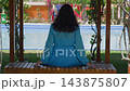 Woman sitting on bench under pergola facing pool, rear view 143875807