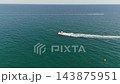 An aerial drone view of a motorboat riding high-speed waves near the town of Lloret de Mar on the Costa Brava, Spain, on a sunny summer day. 143875951