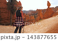 Back view female hiker trekking up dusty footpath among orange sandstone hoodoos with walking sticks, enjoying scenic journey through bryce canyon national park in utah state 143877655