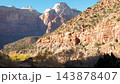 Majestic red rock cliffs of zion national park towering over scenic valley roadway while tourists in passenger vehicles travel beneath clear blue desert skies during autumn evening. Pov in vehicle 143878407