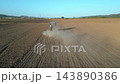 Aerial view of tractor plowing brown field with dust trail and long shadow. Drone footage of agricultural work, soil cultivation and farming on vast farmland. High quality 4k footage 143890386