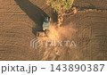 Aerial view of tractor plowing brown field with dust trail and long shadow. Drone footage of agricultural work, soil cultivation and farming on vast farmland. High quality 4k footage 143890387