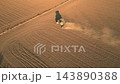 Aerial view of tractor plowing brown field with dust trail and long shadow. Drone footage of agricultural work, soil cultivation and farming on vast farmland. High quality 4k footage 143890388