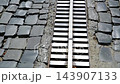 Linear Stormwater Drainage Channel with Metal Grate Installed Along Old Cobblestone Road for Rainwater Collection 143907133