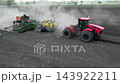 Aerial view of a powerful tractor pulling a large seed drill across a dusty agricultural field. Modern farming machinery performs mechanized sowing during the planting season. 143922211
