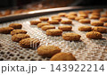 Golden oatmeal cookies move along a conveyor belt at an industrial bakery. Close-up of freshly baked biscuits during automated food production at a large manufacturing facility. 143922214