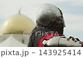Dramatic close view focuses on crusader warrior in iron helmet and mail coif overlooking golden Islamic dome and minaret during historical crusade reenactment. 143925414