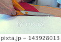 Hand cutting red fabric with scissors on wooden table, crafting process visible 143928013