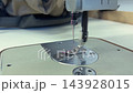 Sewing machine needle in motion stitching fabric on work surface with tools 143928015
