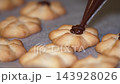 Baker decorates flower-shaped cookies with chocolate icing in kitchen 143928026