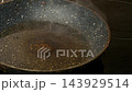 Oil shimmers and forms bubbles around the center of a frying pan heating on a stovetop, with steam rising during cooking 143929514