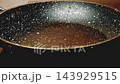 A hand pours oil into a speckled frying pan, where it spreads across the base over several seconds 143929515
