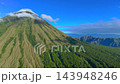 Aerial view of a volcanic mountain slope covered with green forest and clouds under a blue sky in 143948246
