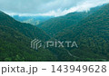 Aerial view of a rural village nestled in a green mountain valley beside a winding road and stream 143949628
