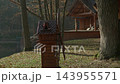 Decorative wooden windmill model spinning in a serene autumn park next to a tranquil lake and rustic wooden cabins 143955571