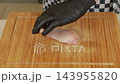 Chef slicing raw chicken breast on a wooden cutting board 143955820