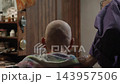 An elderly old man on a wheelchair receives a haircut from his wife at home with a trimmer 143957506