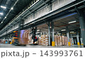 Forklift operators transport palletized goods inside a large industrial warehouse. Workers operate material handling equipment during logistics and distribution center operations. 143993761