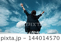 青空に向かって両手を広げる女性の後ろ姿 144014570