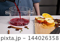 Mulled wine preparation in a bright home kitchen, pouring red wine into a glass pot 144026358
